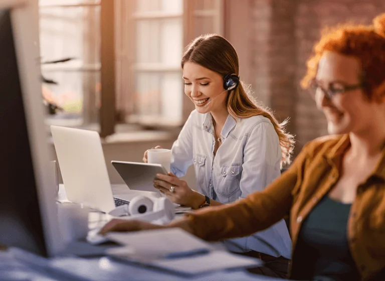 Two women at computers in an office, one wearing a headset