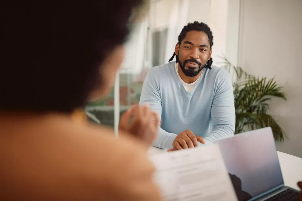 Man at a desk in a meeting, seen past a colleague