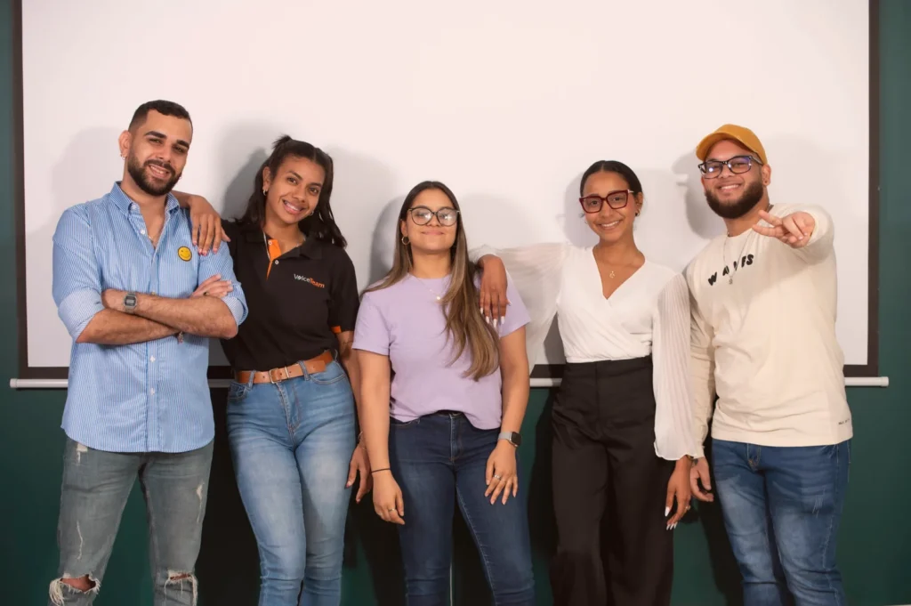 Five VoiceTeam colleagues standing together in front of a wall