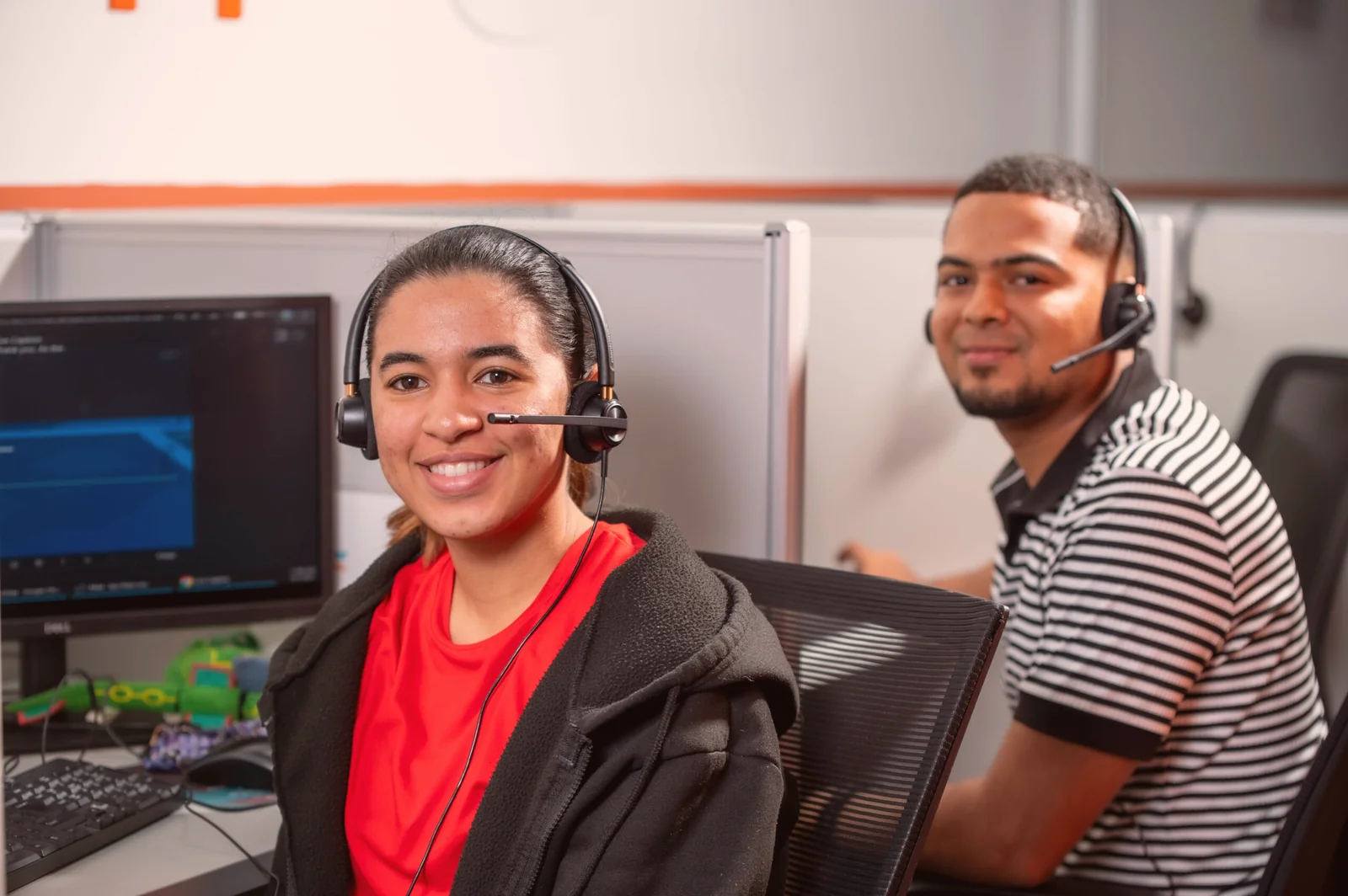 Two smiling agents wearing headsets at their workstations