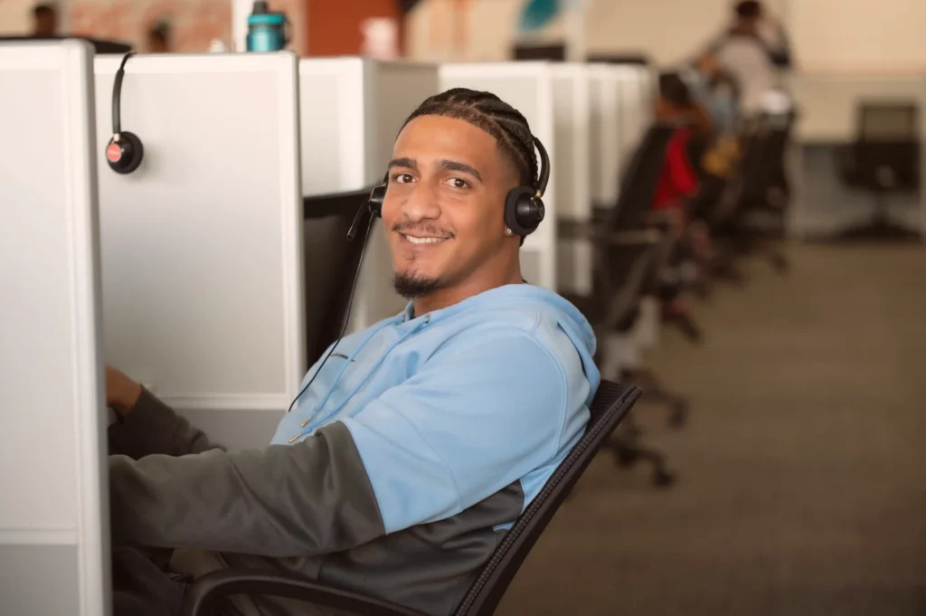 Smiling man wearing a headset, seated at a contact-center workstation