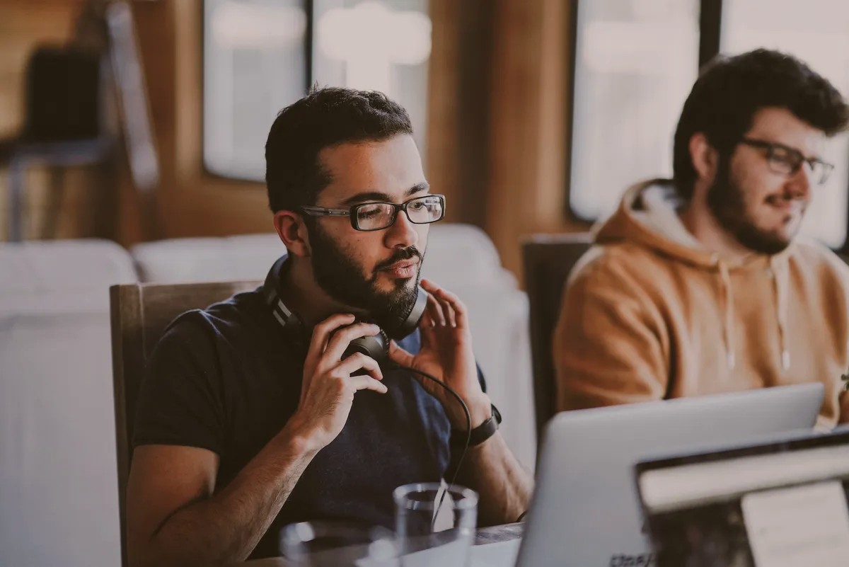 Two men at laptops, one wearing headphones