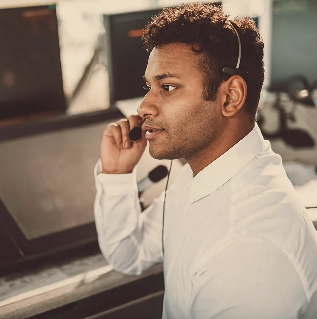 Man in a white shirt talking on the phone at a computer