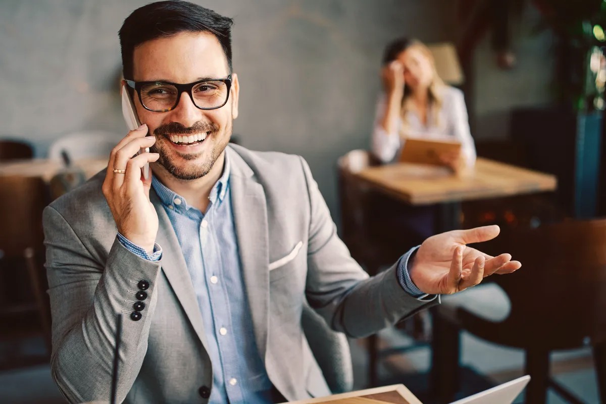 Smiling man in glasses talking on a mobile phone at a table