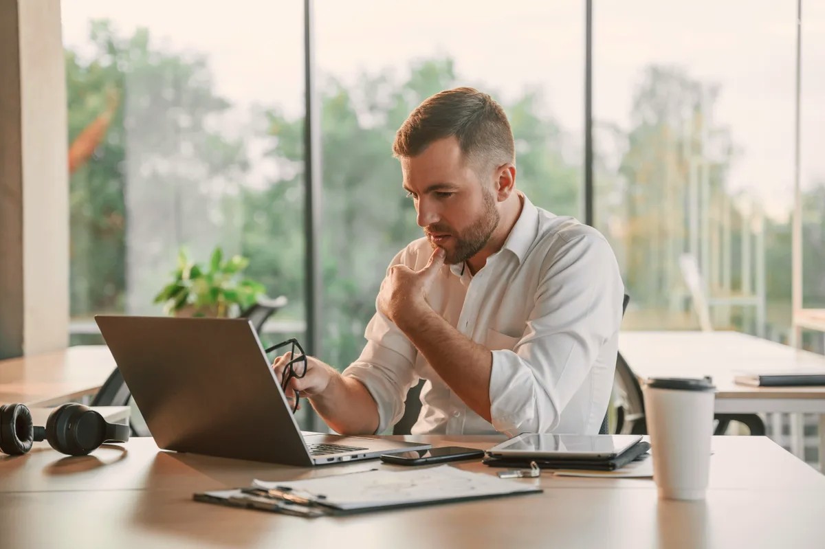 Man in a white shirt reviewing notes beside a laptop
