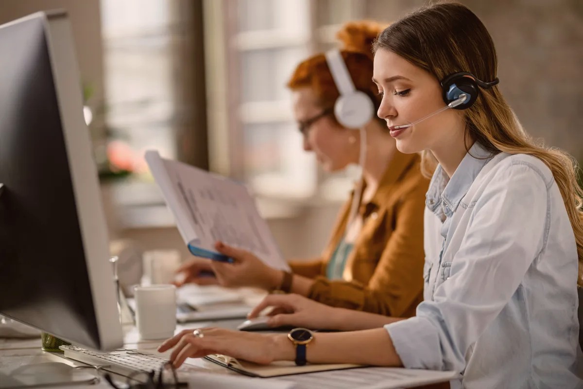 Two women wearing headsets working at computers in an office