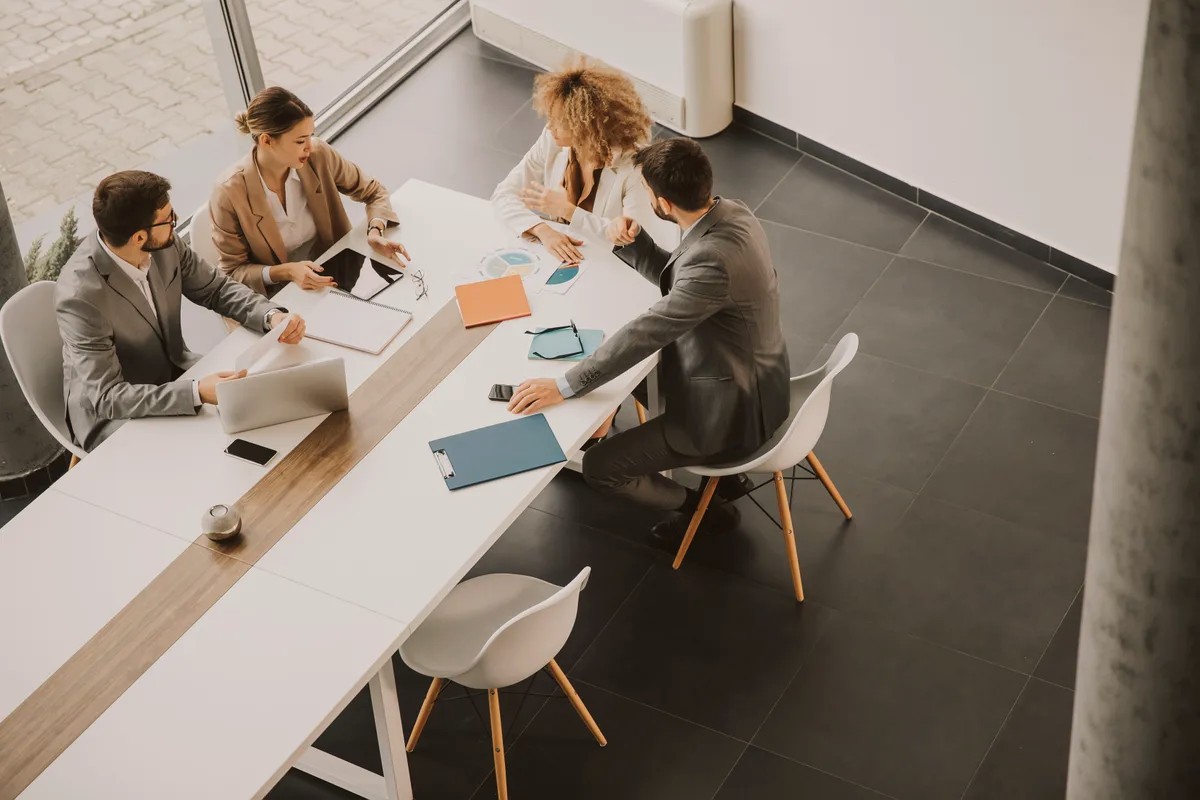 Overhead view of four people meeting at a long white table