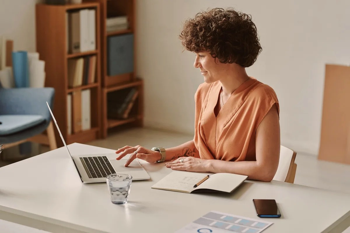 Woman with curly hair working on a laptop at a white desk