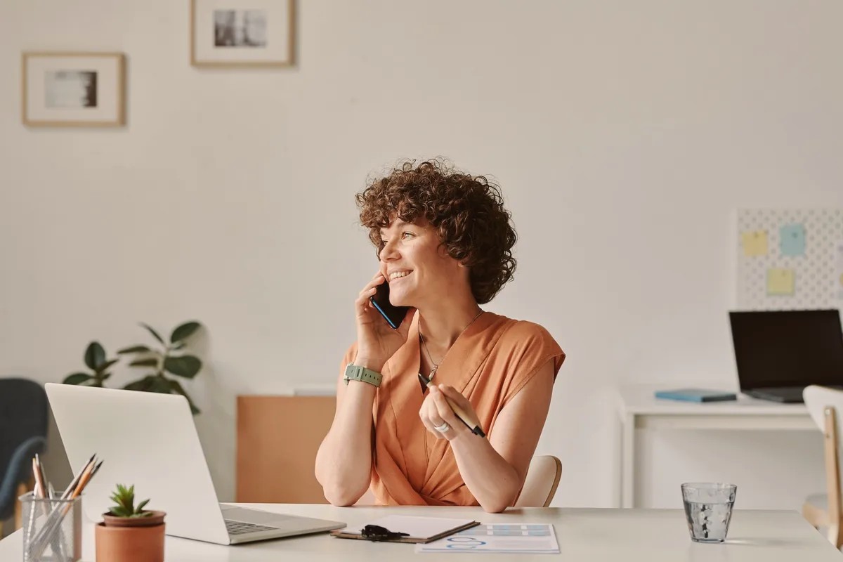 Woman with curly hair talking on a mobile phone at a desk