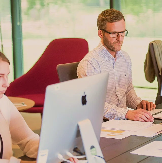 Man in glasses working at a desk with a computer in a meeting room