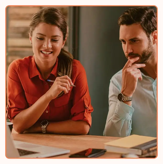 Two colleagues at a desk, one smiling and taking notes