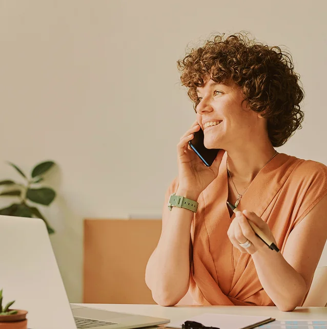 Woman with curly hair talking on a mobile phone at a desk