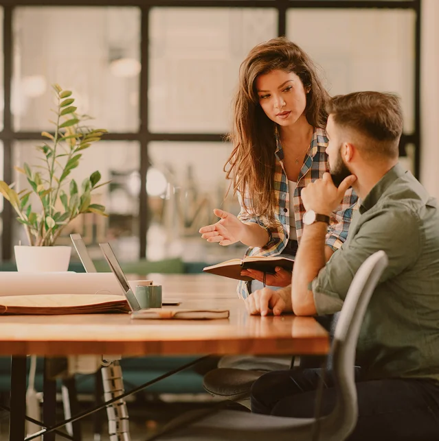Two colleagues talking at a table in an office