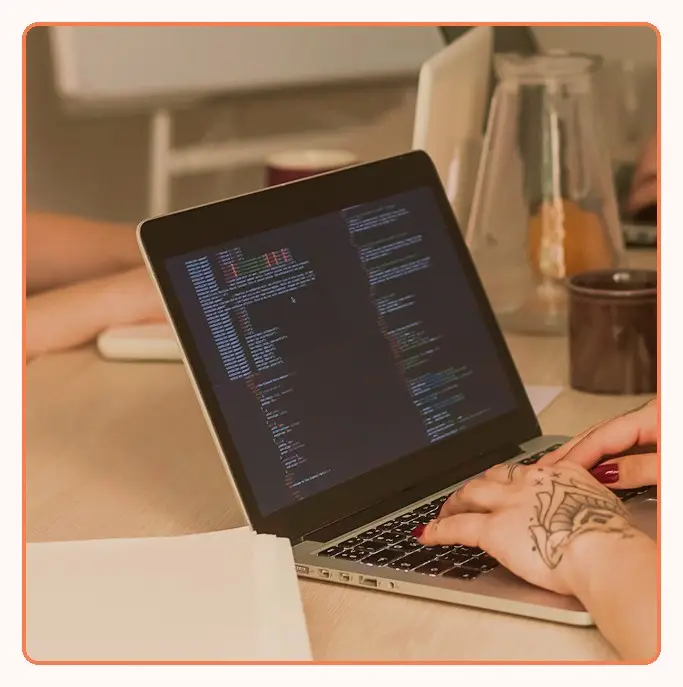 Hands typing code on a laptop at a shared desk