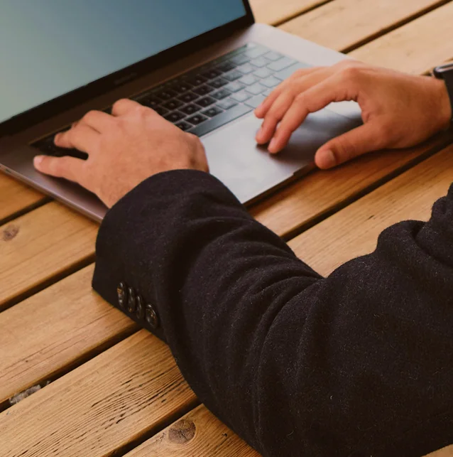 Close-up of hands typing on a laptop on a wooden table