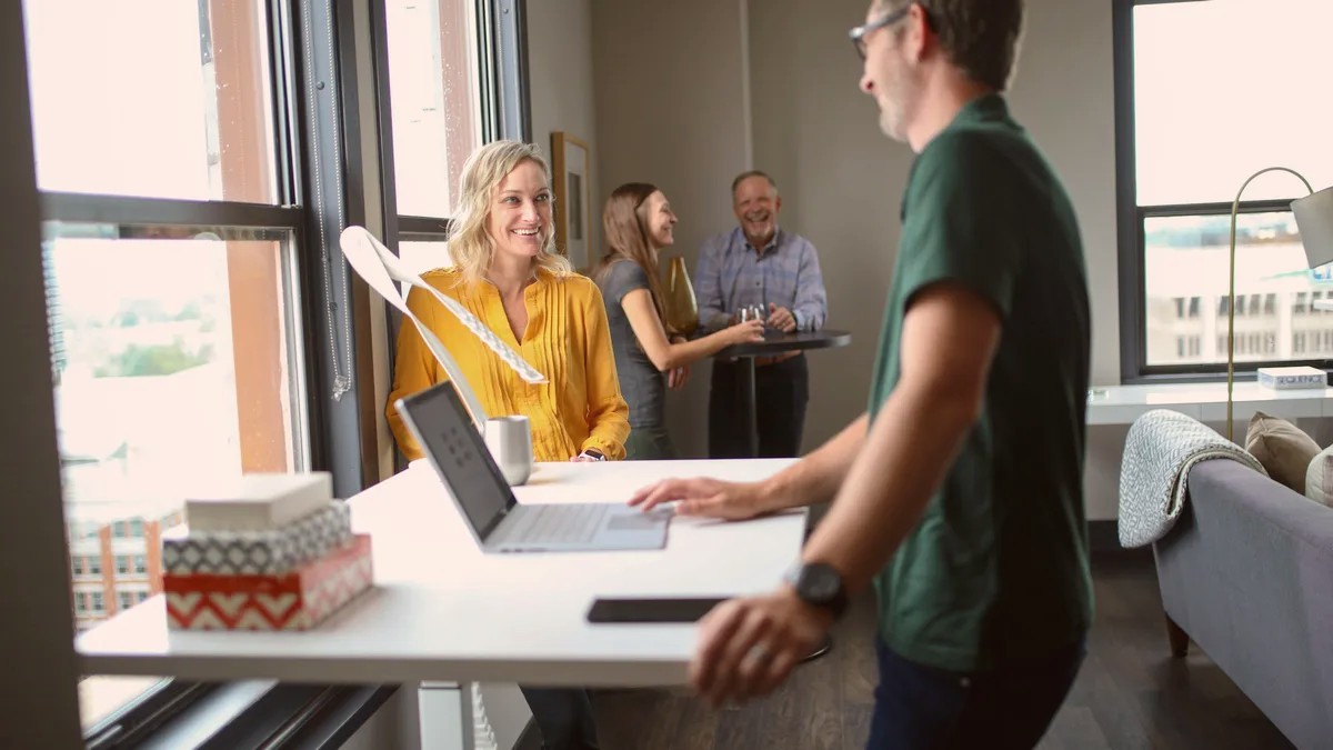 A man standing at a desk talking with colleagues in a bright office