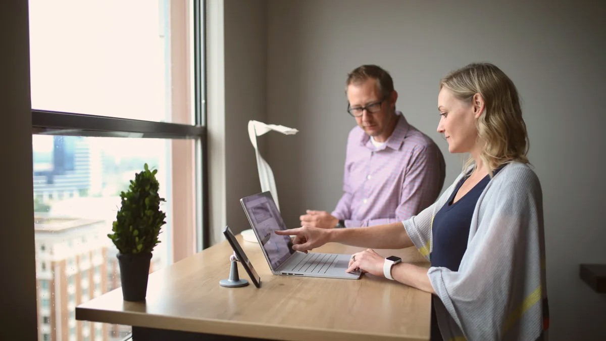 A man and a woman talking at a desk by a window