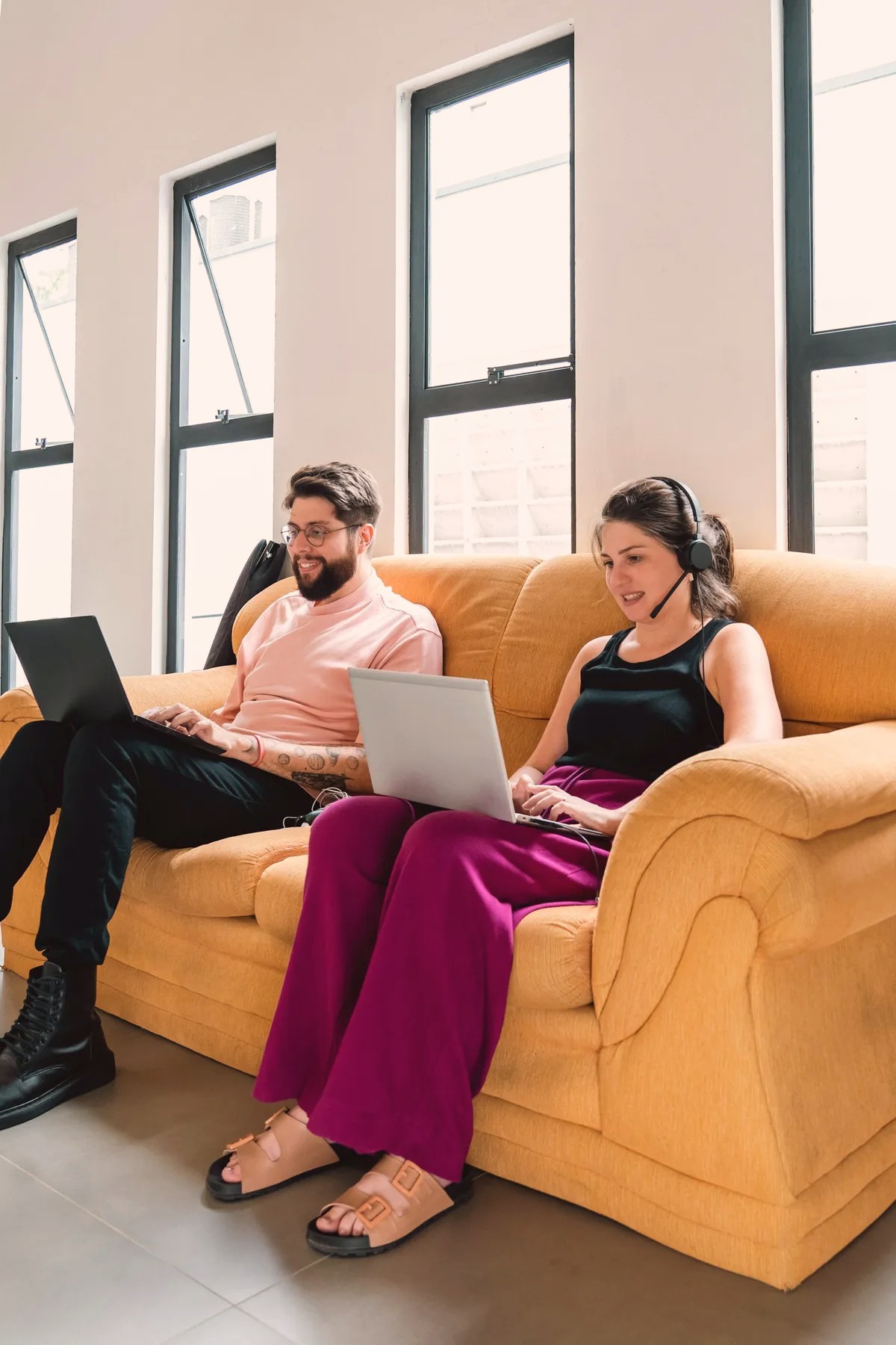 Two people working on laptops on a yellow sofa
