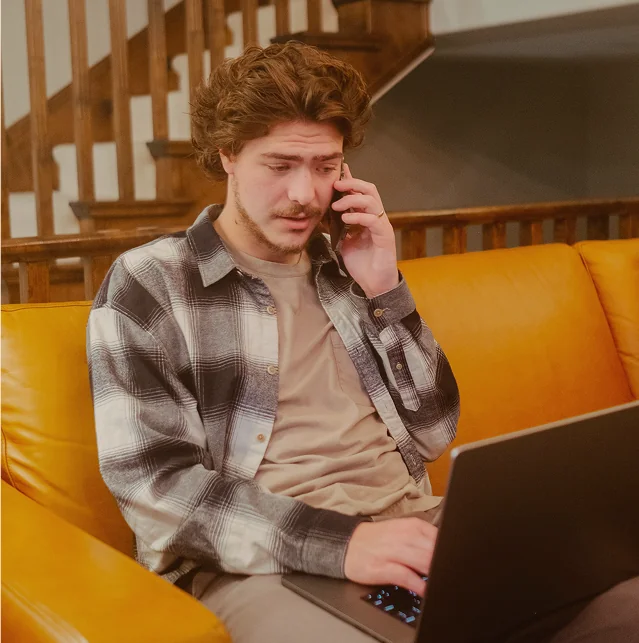 Man on the phone with a laptop on a yellow sofa